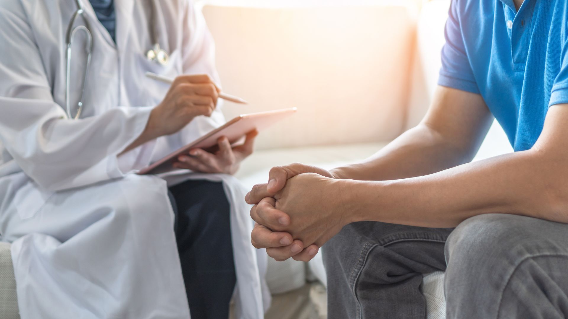 a doctor is talking to a patient who is sitting on a couch .